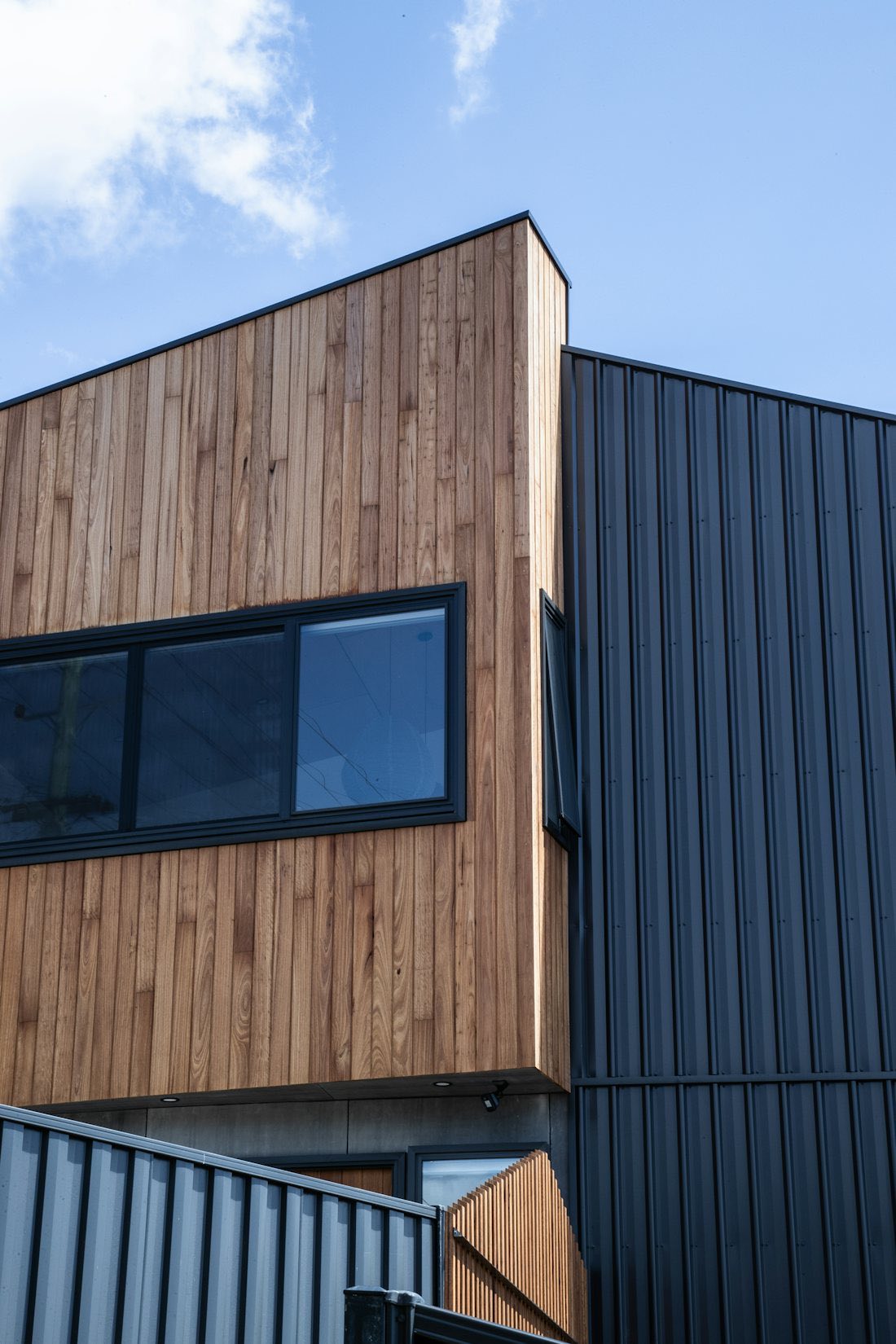Vertical timber cladding beside anthracite panels and a dark framed window on a modern building